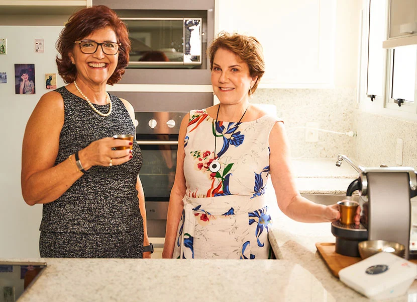 Duas senhoras sorrindo e conversando, junto de seus aparelhos da Telehelp